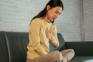 : A woman sitting on a couch holding her chest because of GERD symptoms